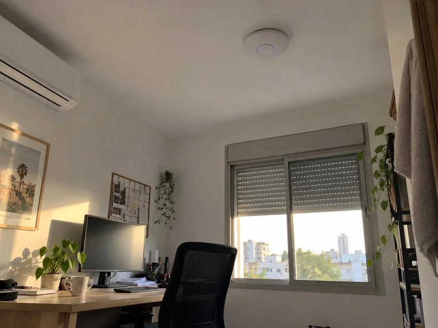 נקודת גישה אלחוטית לבנה בתקרה של פינת עבודה ביתית עם שולחן עץ, מסך ועציץ