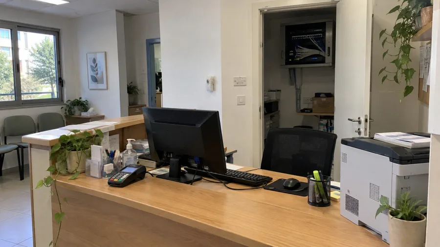 דלפק קבלה של עסק קטן עם מחשב, מסופון אשראי ומדפסת, ובחדר שמאחוריו ארון קטן על הקיר